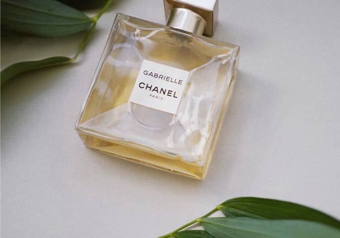 A bottle of golden chanel perfume on a table, surrounded by greenery